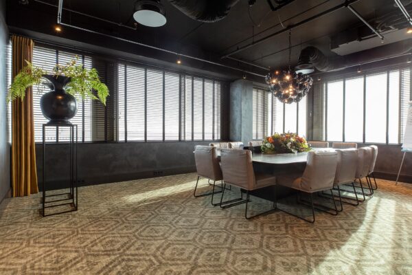 Vergaderruimte aan de Vliegend Hertlaan met een grote ovale tafel, moderne stoelen, sierverlichting en bloemstuk als middelpunt.